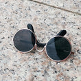 Load image into Gallery viewer, Metallic gold-framed round sunglasses with black lenses on stone surface