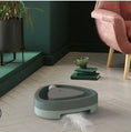 Load image into Gallery viewer, Green triangular turntable cat toy placed near armchair with feather toy on floor