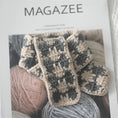 Load image into Gallery viewer, Close-up of gray-beige plaid knitted scarf on a magazine cover featuring yarn balls