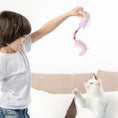 Load image into Gallery viewer, Child playing with a white cat using a pink plush dinosaur-shaped cat toy inside a living room