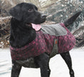 Cargar la imagen en la vista de la galería, Black dog with tongue out wearing a pink camo-patterned and gray waterproof winter jacket in snowy conditions