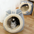 Load image into Gallery viewer, Plush gray and cream cat cave with bunny-like ears and dangling ball, with a gray and white cat lying inside on a wooden floor.