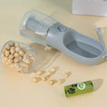 Load image into Gallery viewer, Portable dog feeder bottle lying flat with detachable food container spilling dry kibble and green dog waste bag roll nearby