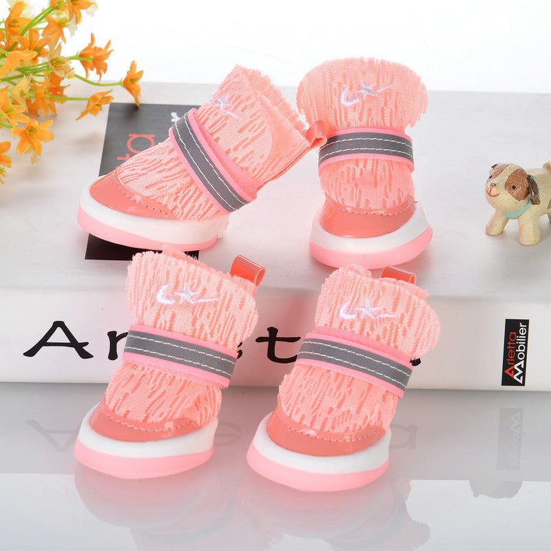 Pink knit dog booties with white soles and reflective strap arranged on display