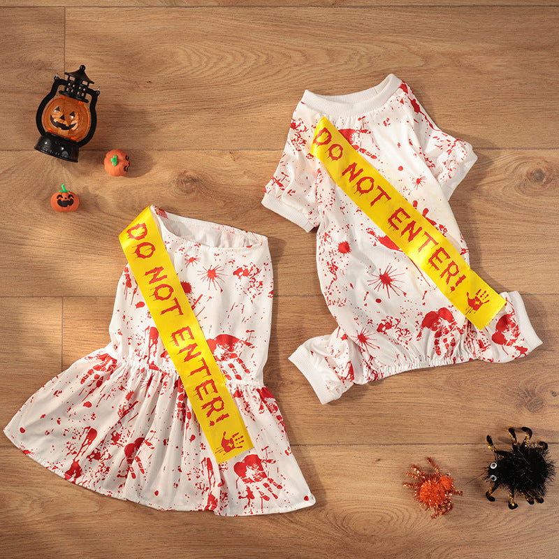 Flat lay of two white blood splatter pet costumes with yellow Do Not Enter sashes on wooden floor with pumpkin decorations