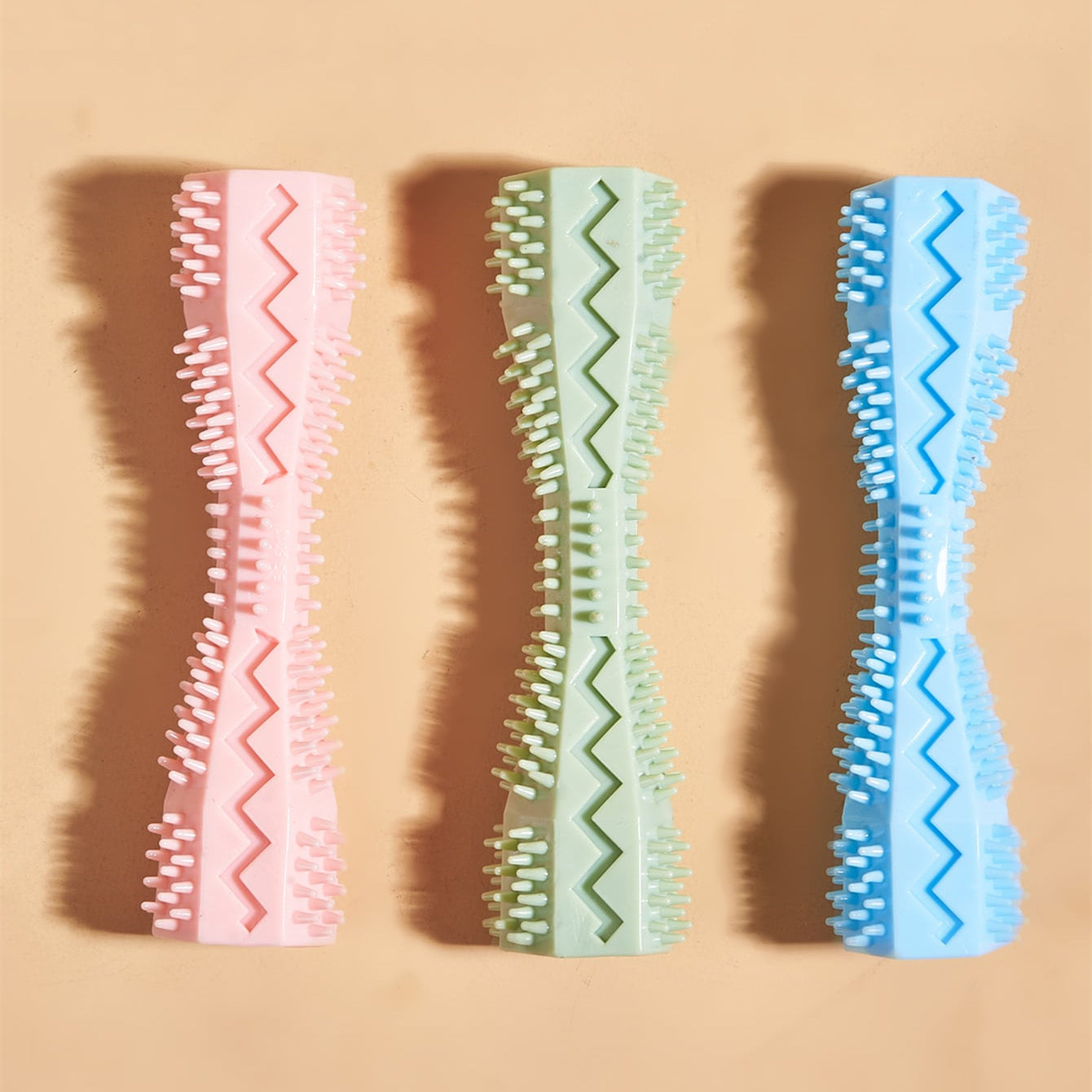 Three pastel-colored dog chew toys in pink, green, and blue with textured bristles and zigzag patterns