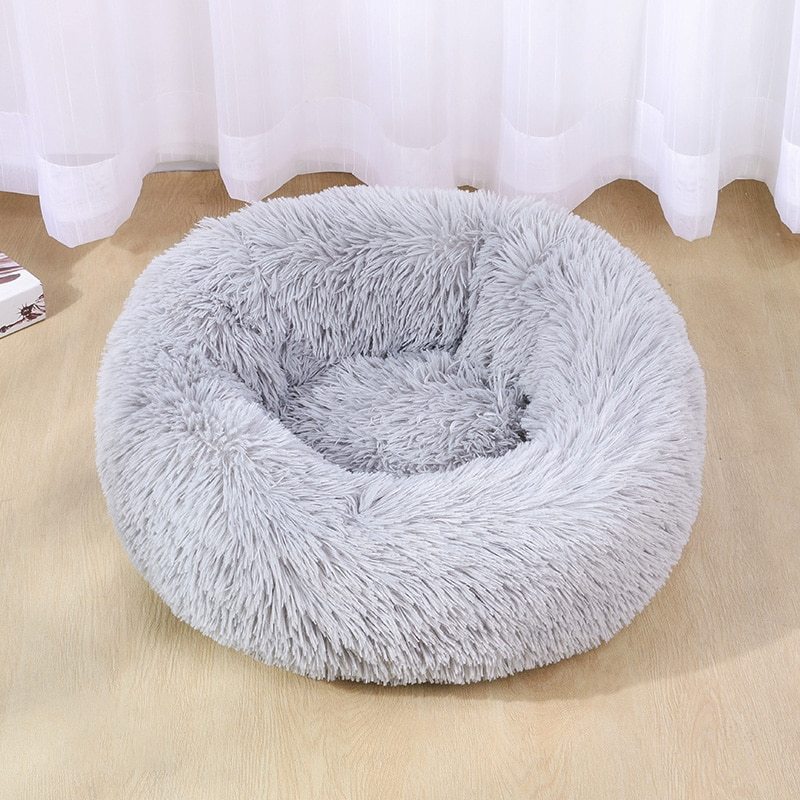 Light gray soft plush pet bed with high bolstered walls on light wooden floor under window