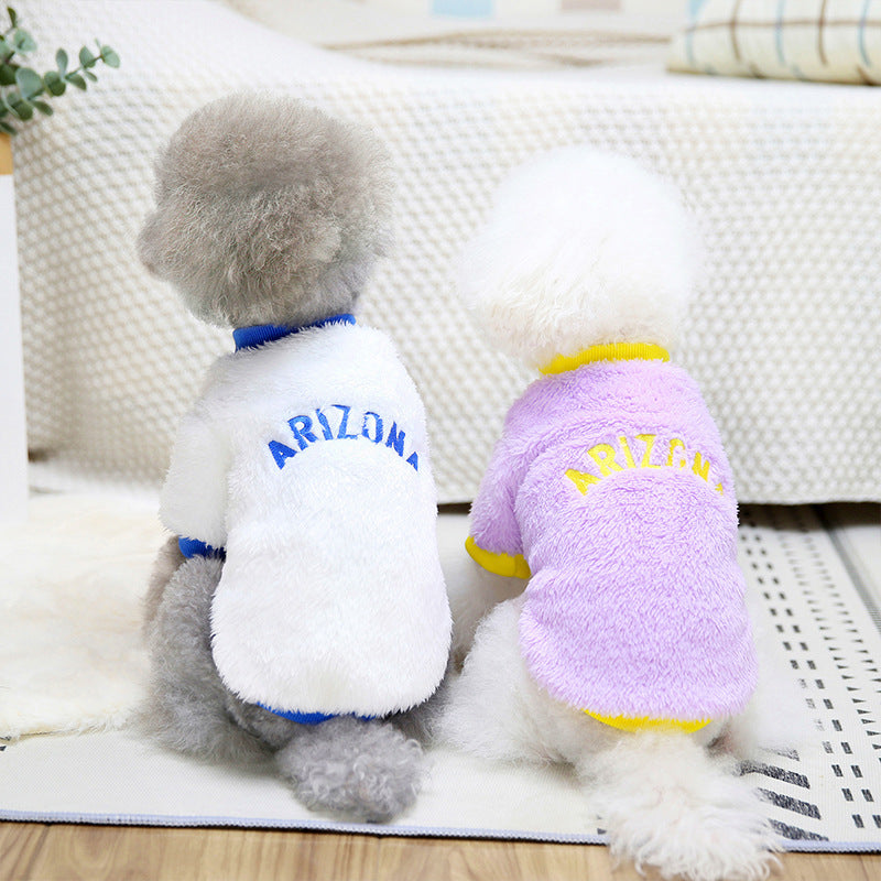 Two small dogs wearing Arizona fleece dog jumpers, one white with blue trim, the other lavender with yellow trim, sitting with backs facing camera