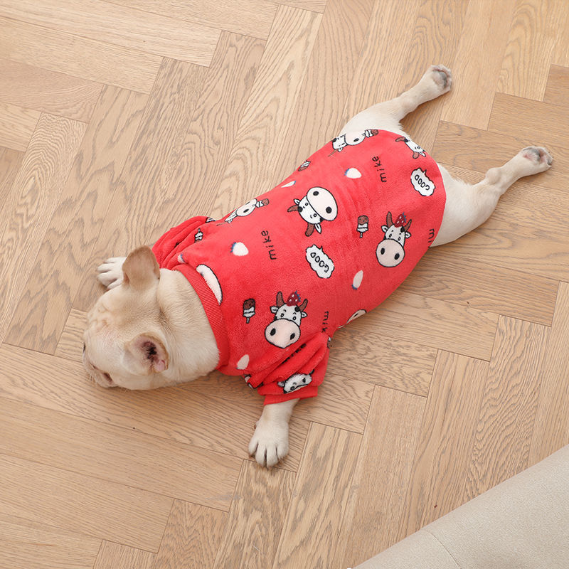 French bulldog laying flat on wooden floor wearing red plush pajamas with cow cartoon prints