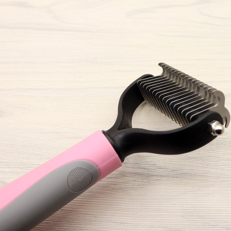 Pink and grey handled dog comb with stainless steel blades on a light wooden surface
