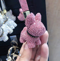 Charger l'image dans la visionneuse de la galerie, Hand holding pink crystal dog keychain with crystal-studded wrist strap in front of assorted crystal charms
