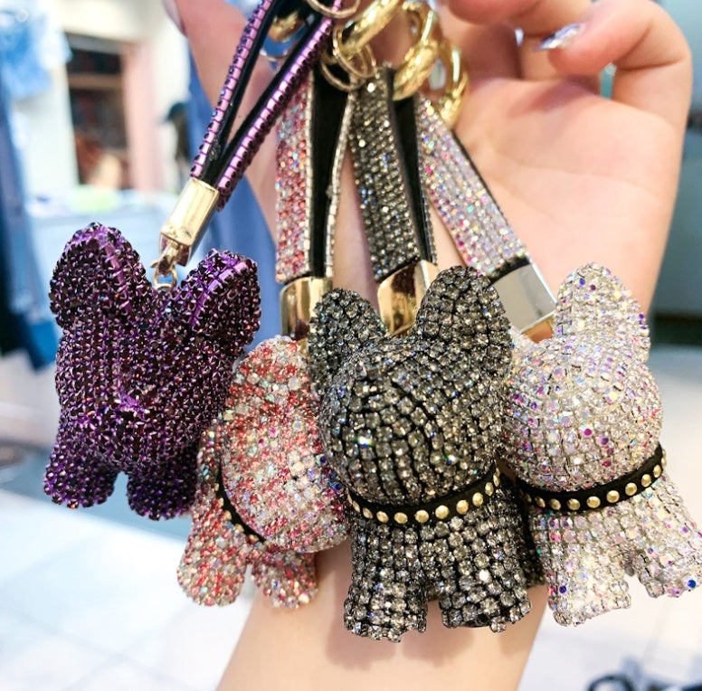 Hand holding several crystal dog keychains in multiple colors showing close-up of textured crystal stones