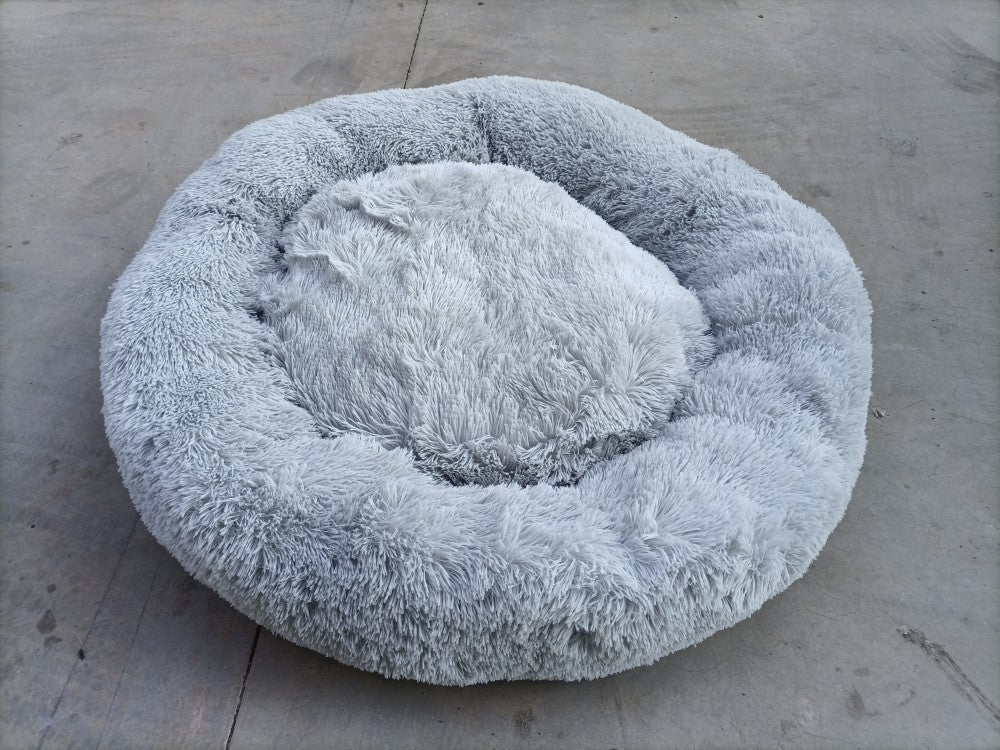 Light gray plush round pet bed on concrete surface showing fluffy texture