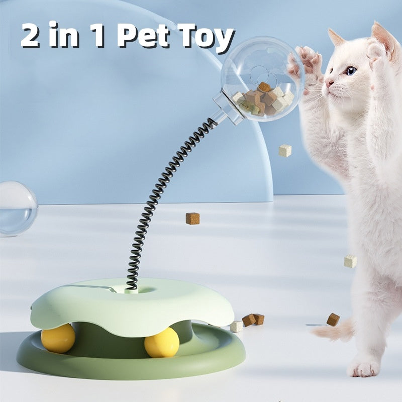 Cat playing with interactive treat toy featuring a green base, spring stem, and clear treat container