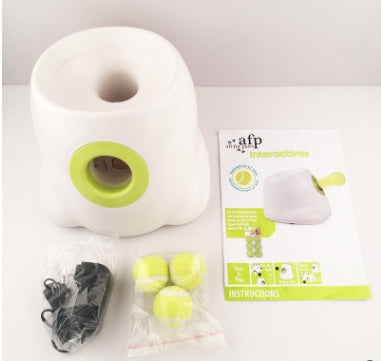 Ball launcher with power adapter, three yellow tennis balls, and instruction manual displayed on white surface