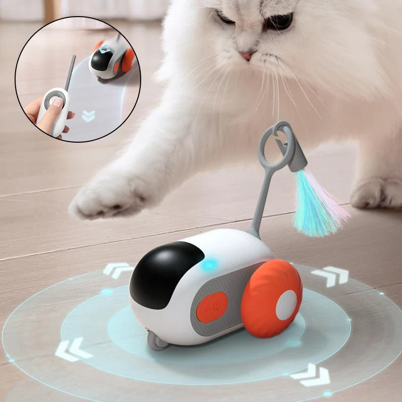 White and black remote-controlled cat toy with orange wheels and colorful feather attachment being chased by a white cat