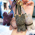 Charger l'image dans la visionneuse de la galerie, Hand holding a cluster of sparkling dog keychains in purple, pink, black, and white crystal designs with gold keyrings
