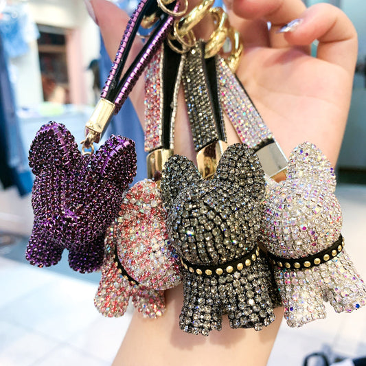 Hand holding a cluster of sparkling dog keychains in purple, pink, black, and white crystal designs with gold keyrings