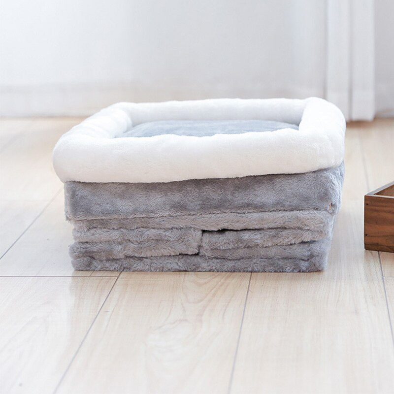 Folded gray plush cat cave with white trim showing compact storage on light wood floor