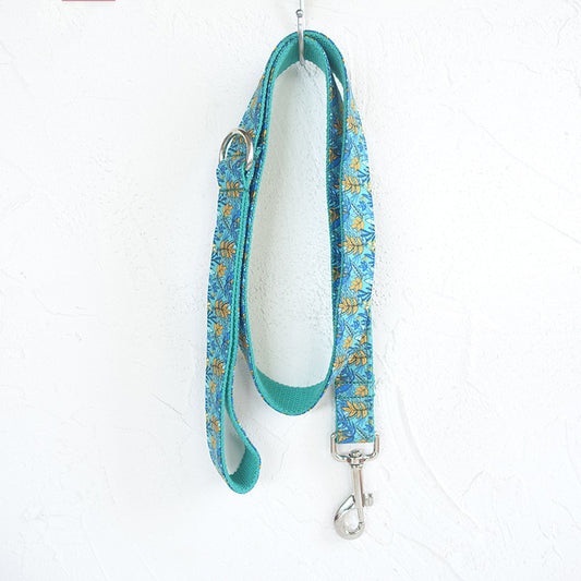 Full view of teal floral patterned dog leash hanging on white textured wall