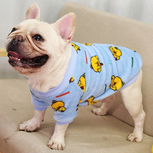 Smiling dog in blue coral fleece pajamas with yellow duck print, standing sideways on couch