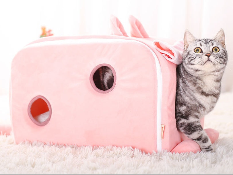 Grey tabby cat exiting pink rectangular bunny shaped cat nest with small circular openings