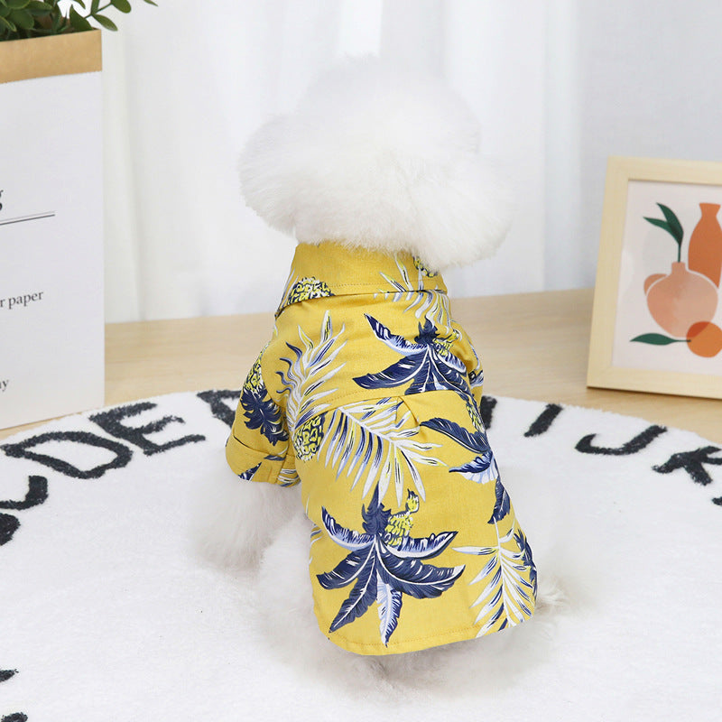 White fluffy dog wearing a yellow Hawaiian leaf print shirt sitting on a rug
