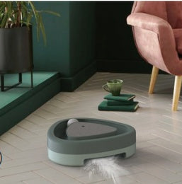 Green triangular turntable cat toy placed near armchair with feather toy on floor