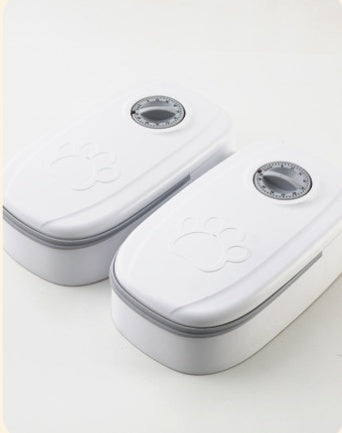 Two white automatic pet feeders with closed lids and paw-print embossed covers, viewed from above
