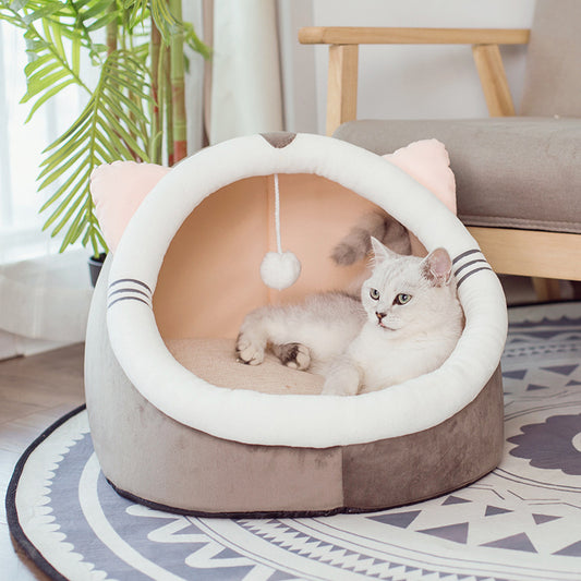 Gray and white plush cat cave bed with cat ears and hanging pompom, cat resting inside