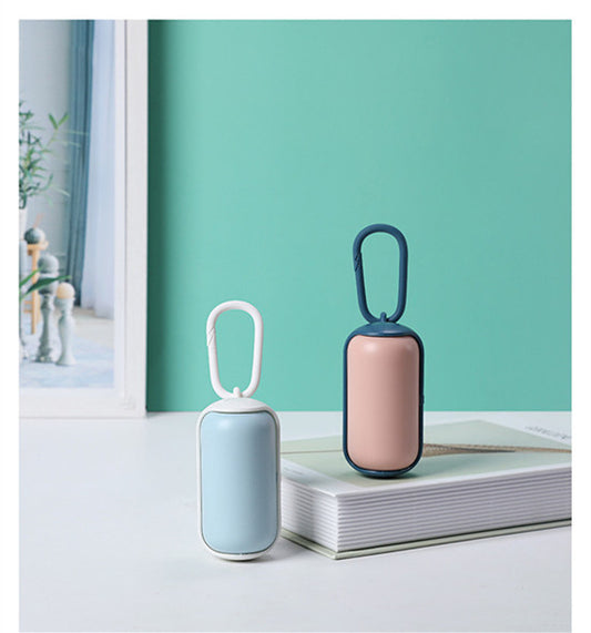 Two pet poop bag dispensers in blue-white and pink-white on a book against green background
