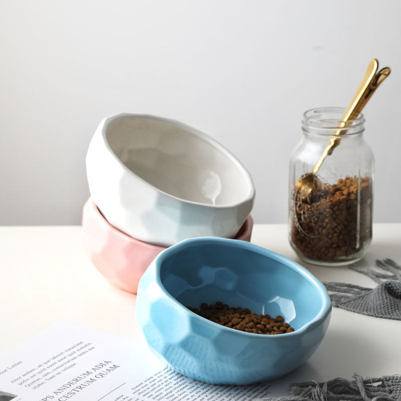 Stacked blue, pink, and white ceramic pet bowls with kibble and gold scoop nearby