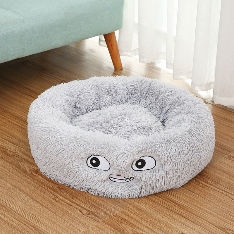 Grey plush round pet bed on wooden floor with animated facial embroidery