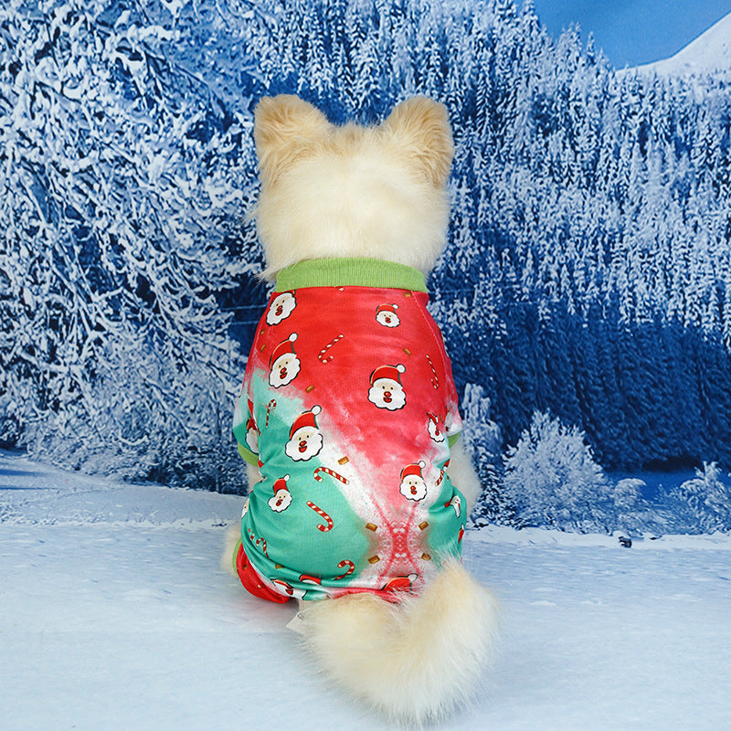 Small dog from behind in green and red pajamas adorned with Santa faces and candy cane prints against a snowy forest background