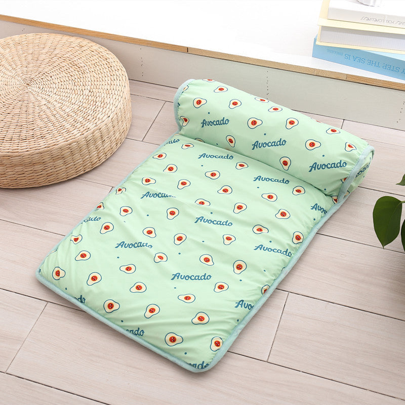 Green cooling pet mat featuring avocado fruit print and attached bolster pillow placed on wooden floor near a woven seat
