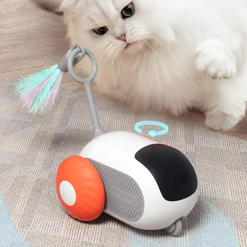 White cat playing with remote control cat toy featuring orange wheels and flexible feather on gray carpet