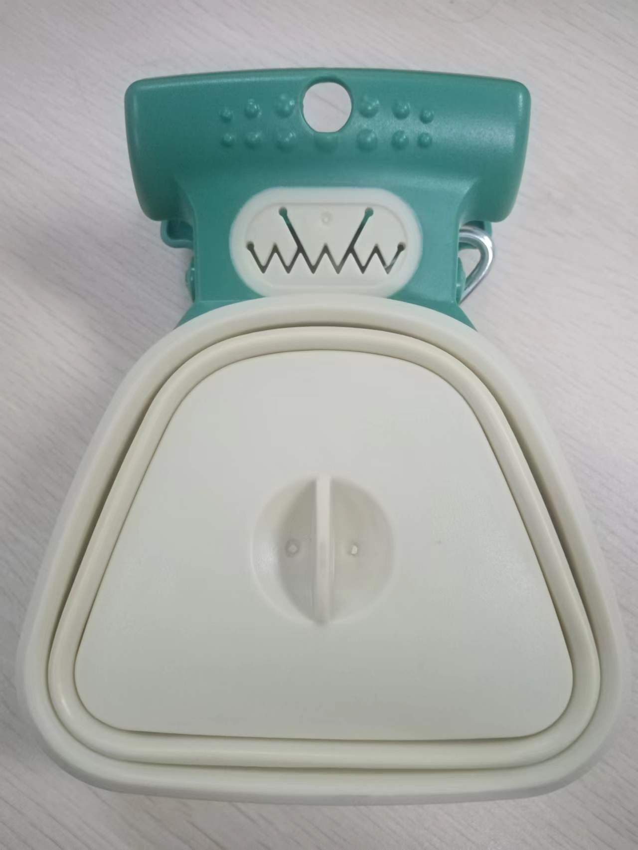 Close-up of teal and white dog poop spoon dispenser showing handle and folding details