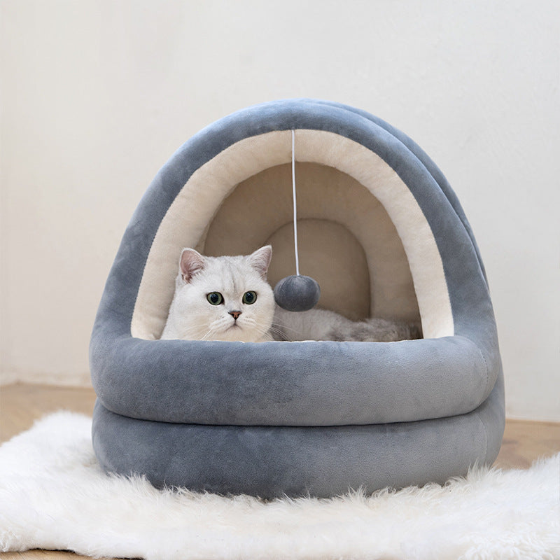 Gray plush pet cave bed with cream-colored interior lined with soft plush material, and a cat resting inside next to a hanging plush ball toy
