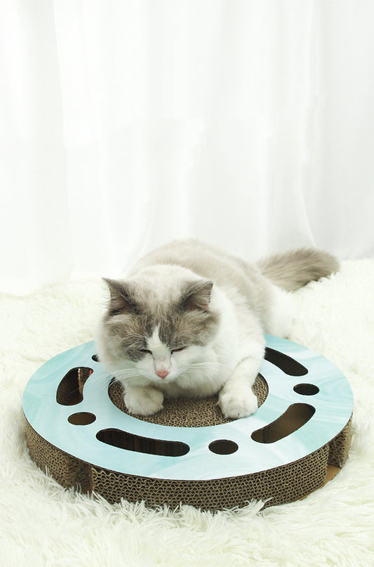Cat resting on a round light blue corrugated paper scratcher with holes and ball