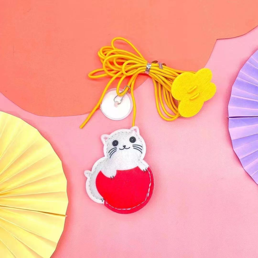 Close-up of felt cat-shaped toy with yellow elastic rope and suction cup on pink background