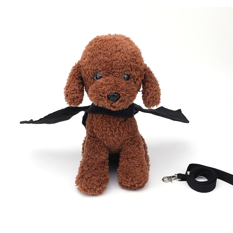 Front view of brown plush toy dog wearing black bat harness and detached leash lying beside it