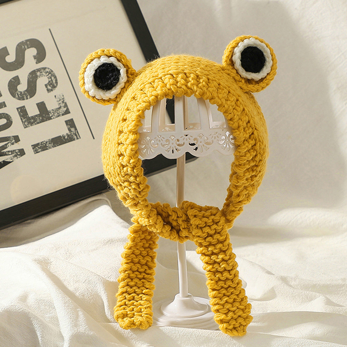 Yellow hand knitted dog hat with playful ear design displayed on white stand