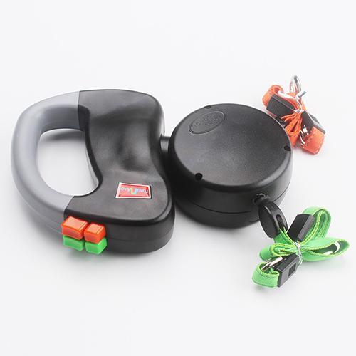 Black and gray ergonomic handle of dual retractable dog leash with orange and green straps shown from top view