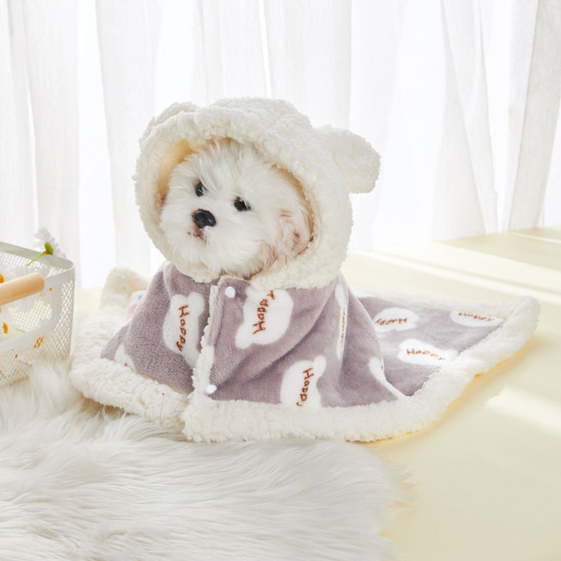 Small white dog wearing gray flannel hooded shawl with 'Happy' cloud designs sitting on white fur rug