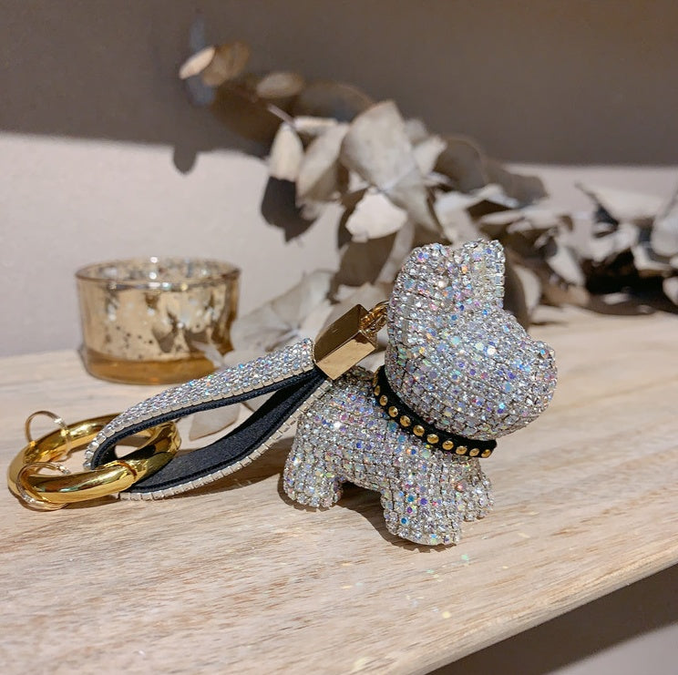 White crystal dog keychain displayed on a light wood surface with golden candle and decorative dried flowers in the background