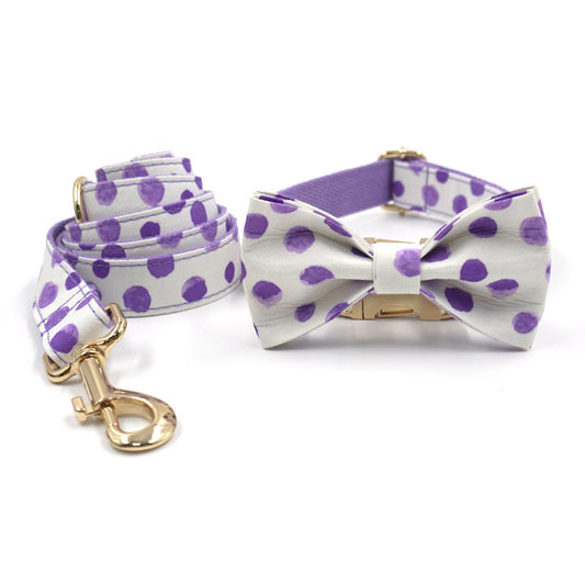 Dog collar and leash set with purple polka dots and attached bow tie, laid flat