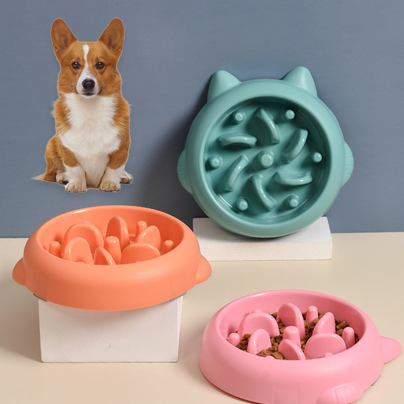 Three interactive slow feeder pet bowls in green, orange, and pink with bone-shaped ridges, dog figure in background