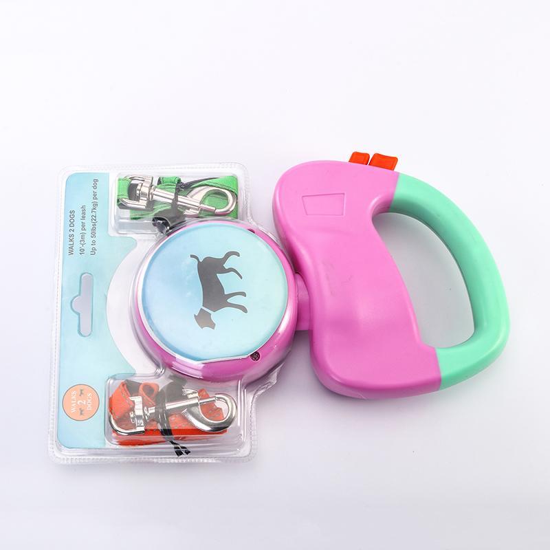 Packaged pink and green dual retractable dog leash featuring blue graphic of dog on spool, with leash clips visible