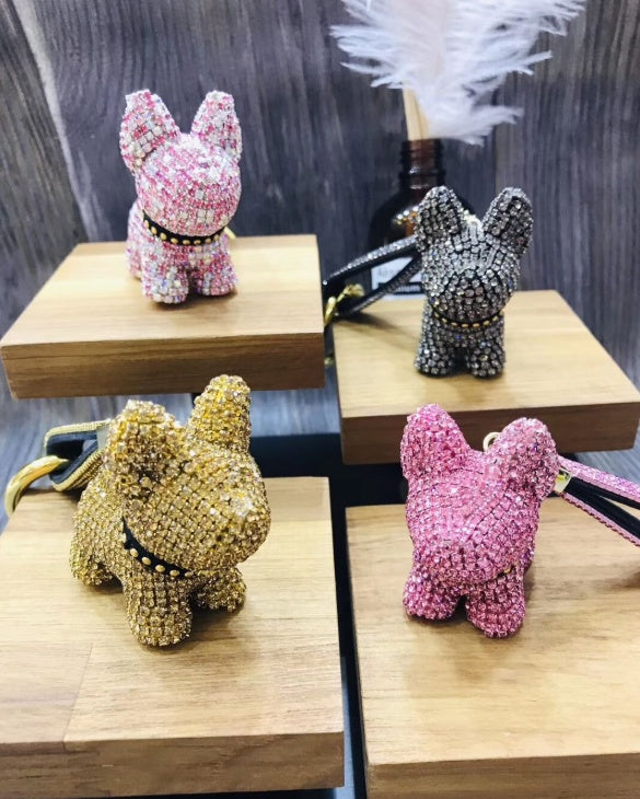 Four crystal dog keychains displayed on wooden blocks in pink, black, gold, and bright pink colors with studded collars