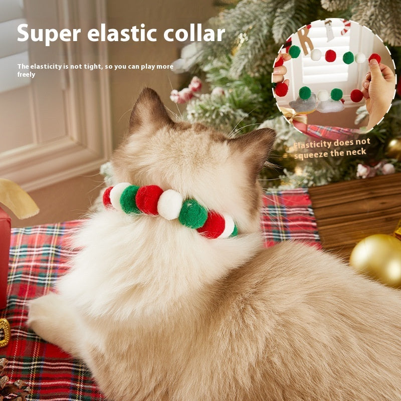 Back view of a cat wearing an elastic Christmas collar with alternating red, green, and white felt balls, showing collar elasticity near a decorated Christmas tree
